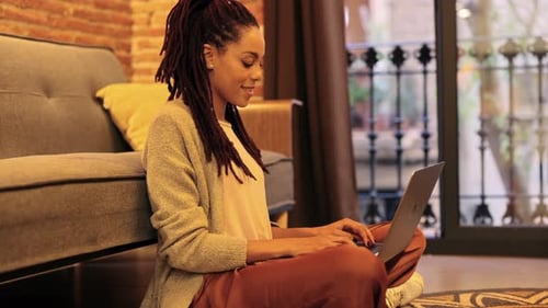 linda mulher afro-americana usando laptop na sala de estar em casa