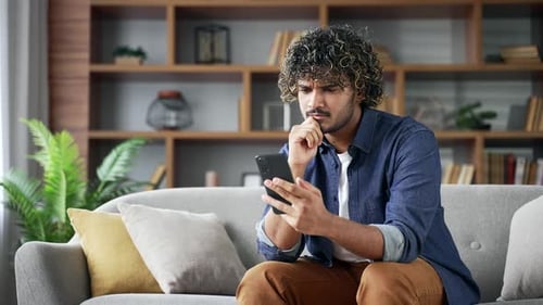 Thoughtful Man Browsing Smartphone on Couch