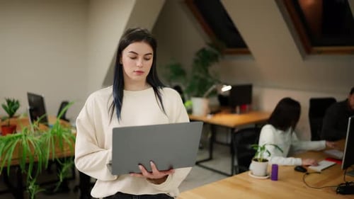 Focused Brunette Woman Walking with Laptop By Office with Coworkers Trying to Solve the Problem