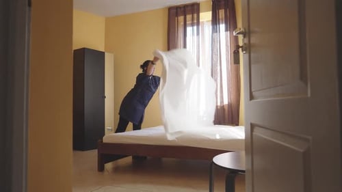 Female Housekeeper Changing Bedding in a Hotel Room