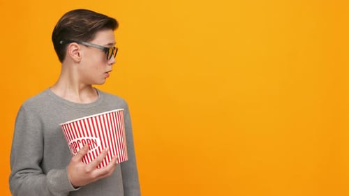 Young Person Holds a Popcorn Bucket While Looking to the Side Against a Bright Yellow Background in