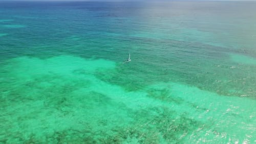 Single sailboat drifting over bright turquoise Caribbean sea