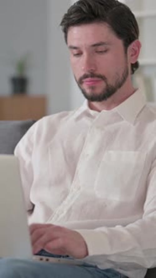 Man with Beard Uses Laptop While Sitting Indoors
