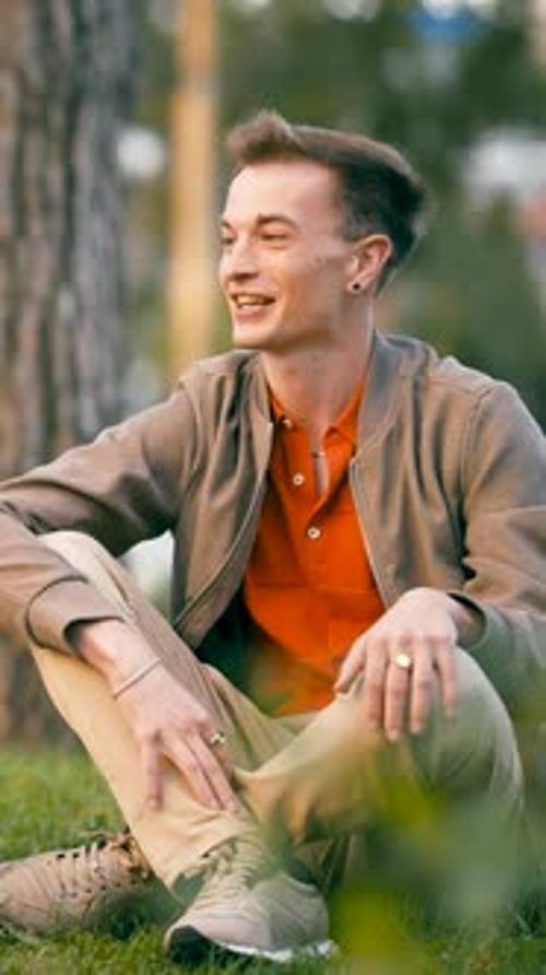 Happy Young Man Relaxing on Green Grass in a Park Vertical
