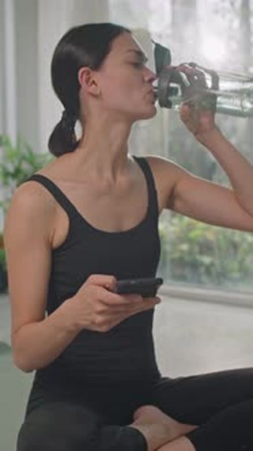 Woman Drinks Water and Uses Phone After Yoga