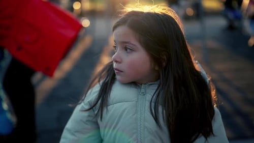 Introspective lonely 8 year old female child seated at park bench observing surroundings in backlit