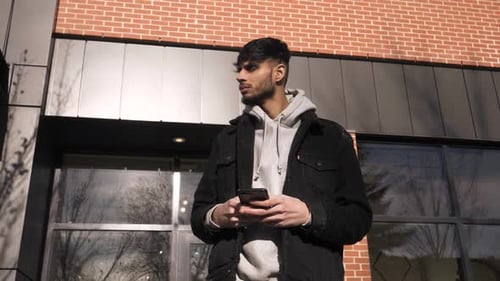 Young Man Using Smart Phone Below Sunny Brick Building Adult