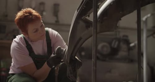 Woman Sands Car Bumper in Auto Body Shop