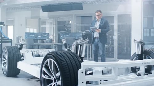 Automotive Design Engineer Looking at Technical Drawing of an Electric Car Chassis Prototype on a T