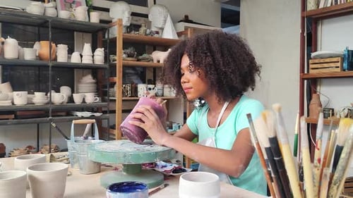 Females potter owners wearing apron sitting and painting a cup ceramics in pottery studio.