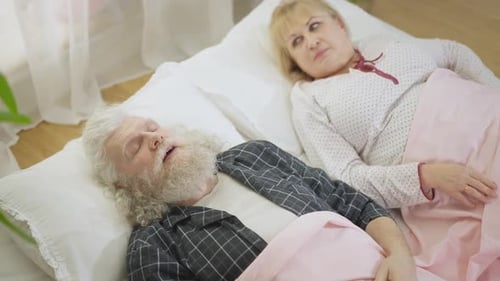 Vue grand angle d'un vieil homme caucasien ronflant, dormant dans son lit, réveillant une femme