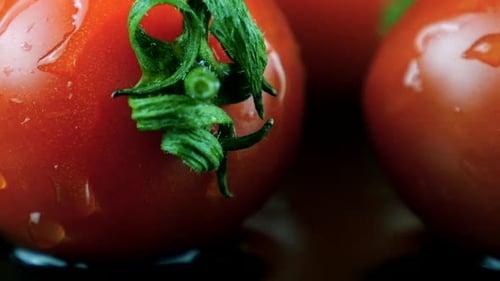 Wassertropfen fallen auf eine rotierende Kirschtomate auf schwarzem Hintergrund.