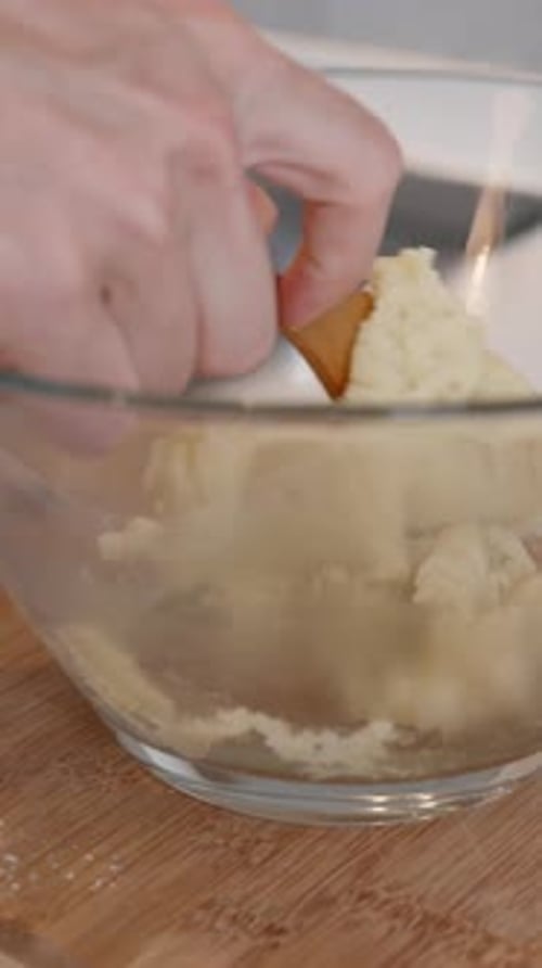 The pastry chef stirs the choux pastry in a large glass bowl, close-up view. Vertical video.