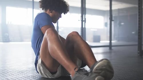 Exercising in gym, man doing sit-ups with medicine ball, focusing on fitness