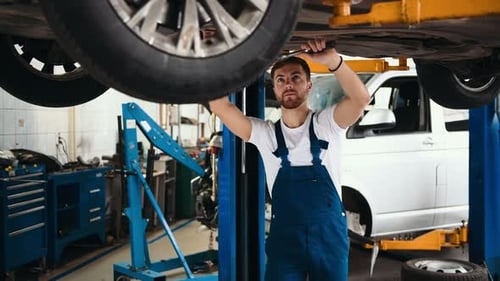 Handsome mechanics in uniform are working in auto service with lifted vehicle. Car repair