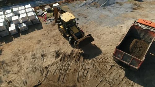 Backhoe Loader Fills Dump Truck at Construction Site
