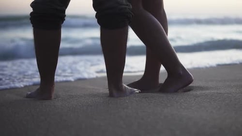 Static slow motion shot of a couple in love standing in the sand on the beach with calm waves from t