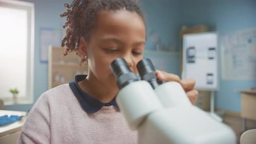 Porträt eines klugen kleinen Schulmädchens, das unter das Mikroskop schaut. Im Klassenzimmer der Grundschule Cu