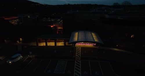 Emergency sign at hospital at night. Red letters against dark sky. Aerial pullback reveal as white v