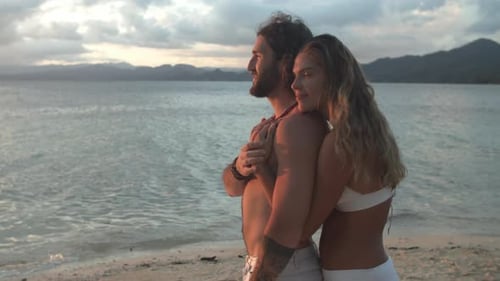 4k video footage of a happy young couple embracing on the beach at sunset