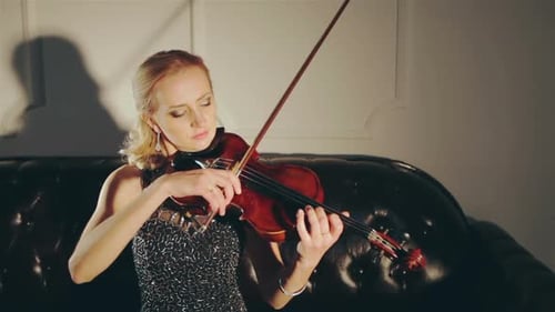 Woman Playing Violin Elegantly on Black Leather Couch