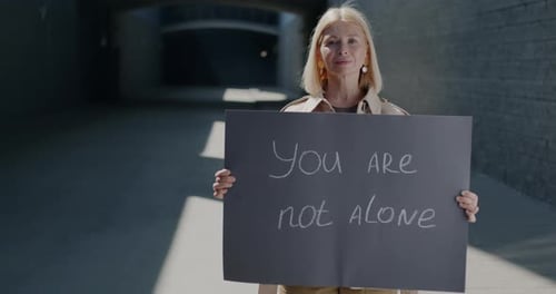 Retrato a cámara lenta de una mujer madura con el cartel de «No estás solo» que expresa solidaridad de pie
