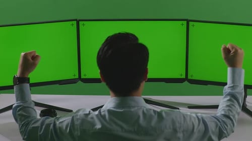 Happy Asian Man Celebrating While Working With Mock Up Multiple Computer Monitor In Green Screen