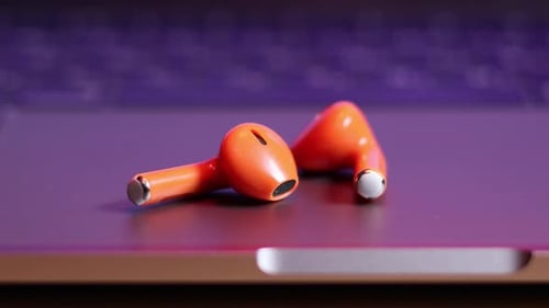 Wireless Orange Earbuds Lying on Laptop Computer
