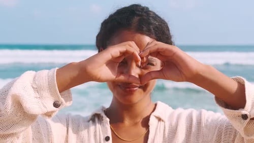 Joven india sonriente mira a la cámara y muestra el corazón parado en Sea Beach