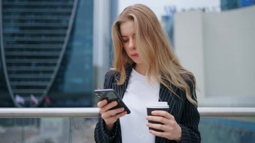 Portrait of Beautiful Blonde Woman in Business Suit with Smartphone and Cup of Coffee in Urban View
