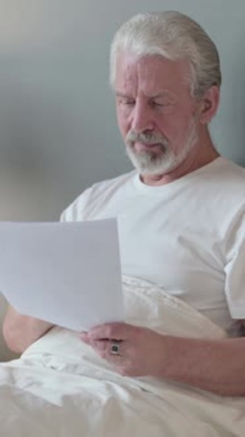 Senior Man Reading Document in Bed, Cheerful Reaction