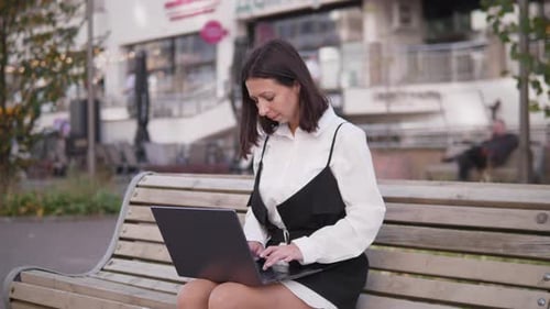 A Young Professional Engaged in Working on a Laptop While Enjoying the Outdoors in a City Park