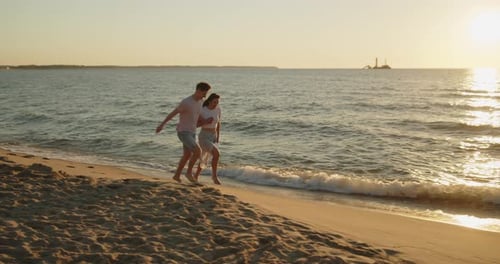 Young Loving Couple Have Fun Running on the Beach at Sunset