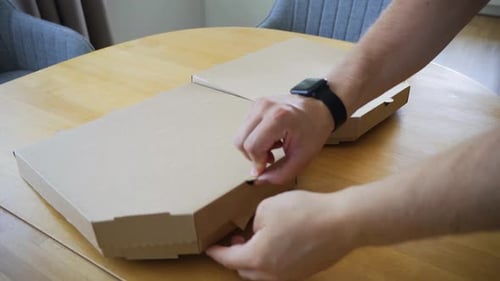 the handheld shot of man's hand opening delivered Italian pizzas in a cardboard box on the table at