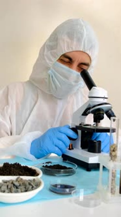 Scientist in Hazmat Suit Examining Sample with Microscope