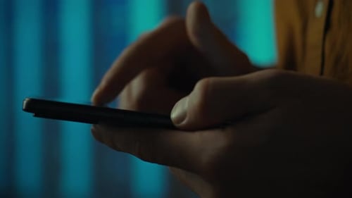 Person using a smartphone with illuminated background in a dimly lit space
