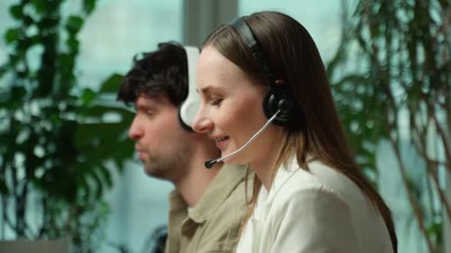 Side View of a Beautiful Young Business Woman and a Handsome Businessman Wearing Headphones Using