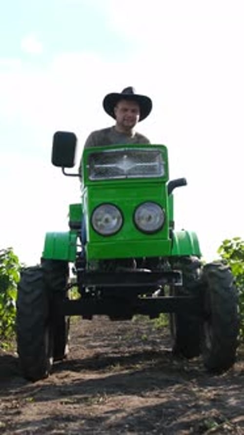 A Man is Driving a Green Tractor As He Navigates Through a Scenic Vineyard Landscape