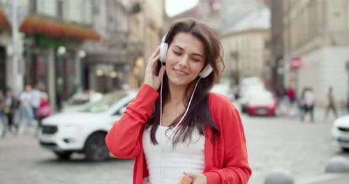 Pretty Young Caucasian Stylish Woman with Dark Hair and in Headphones Walking the Street and
