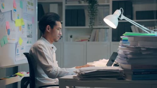 Frustrierter asiatischer Geschäftsmann arbeitet am Tisch am Büroarbeitsplatz.