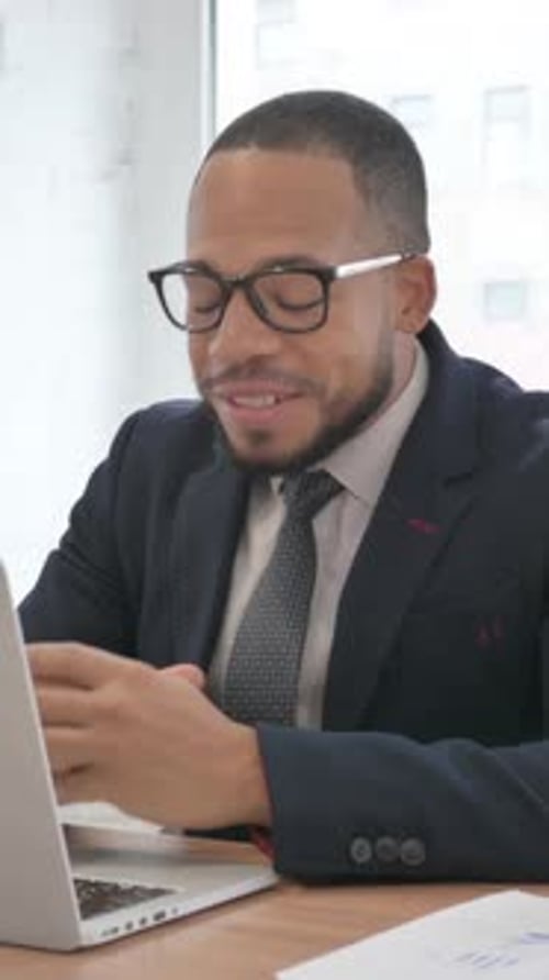 Mixed Race Businessman Chatting Online on Laptop while Sitting in Office, vertical video