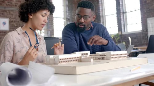 Focused diverse architect colleagues discussing work with building model in office in slow motion