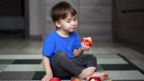 Child Eats Red Apple Sitting on Floor