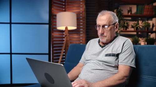 Senior Man Using Laptop on Blue Sofa