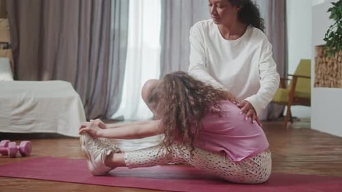 Woman Helps Child Stretch at Home on Yoga Mat
