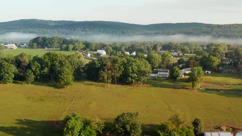 American farmland. Aerial revealing shot of farm and buildings during summer morning fog.