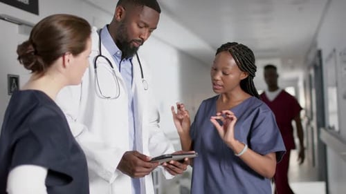 Diverse male and female doctors discussing work, using tablet in corridor at hospital, slow motion