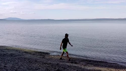 Mature asian man walks on a rugged ocean beach enjoying nature and freedom
