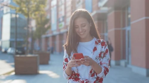 Smiling woman using her phone on a sunny street