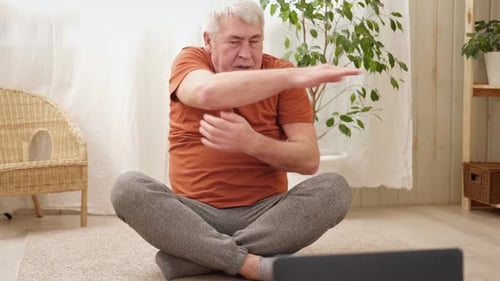 Hombre mayor maduro feliz haciendo ejercicios de gimnasia en casa en línea con una computadora portátil, estilo de vida saludable